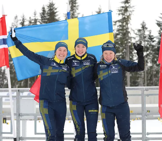 Guldtrion Evelina Wickbom, Elin Schagerström och Lisa Larsen med stora leenden framför den svenska flaggan.