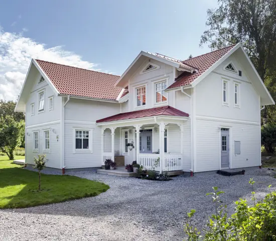 En vit trävilla, tillverkad av Eksjöhus, belägen i en solig trädgård.