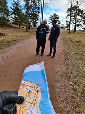 Bild visar en uppförstorad karta i förgrunden och två personer som orienterar.