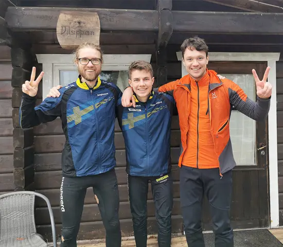 Gustav Bergman, Noel Braun och Nils van der Poel med glada miner utanför stuga.